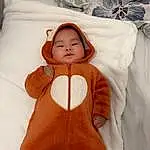 Visage, Peau, Head, Hand, Yeux, Blanc, Comfort, Neck, Textile, Sleeve, Orange, Gesture, Baby & Toddler Clothing, Baby, Thumb, Happy, Linens, Chest, Baby Sleeping, Abdomen, Personne
