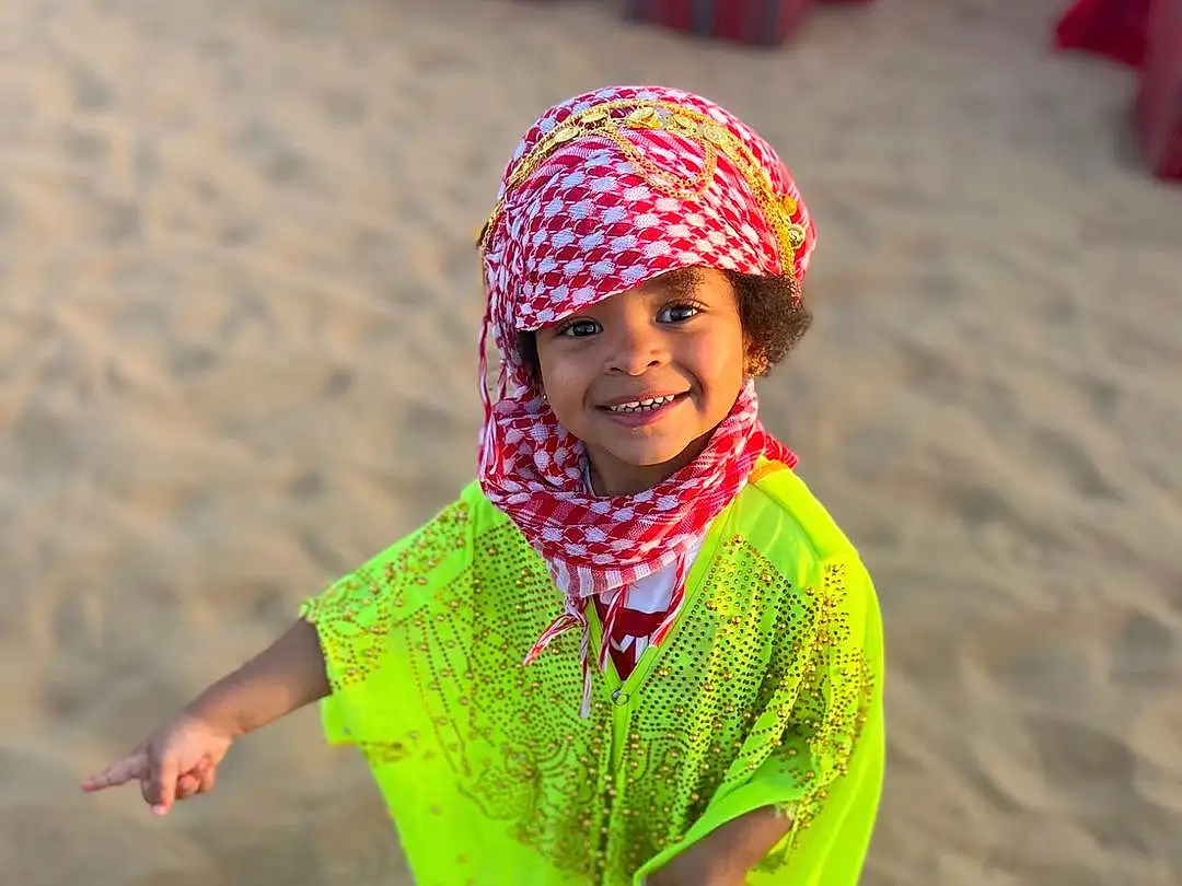 Photograph, Sourire, Light, Green, Natural Environment, People In Nature, Happy, Headgear, Plage, Red, Sand, Bambin, Tints And Shades, Fun, Landscape, Leisure, Recreation, Aeolian Landform, Magenta, Fashion Accessory, Personne, Joy, Headwear